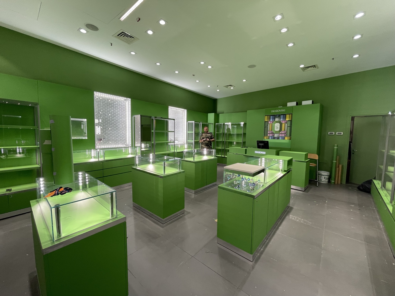 Interno di una boutique Swarovski con pareti e mobili espositivi verdi, teche in vetro e illuminazione a soffitto.