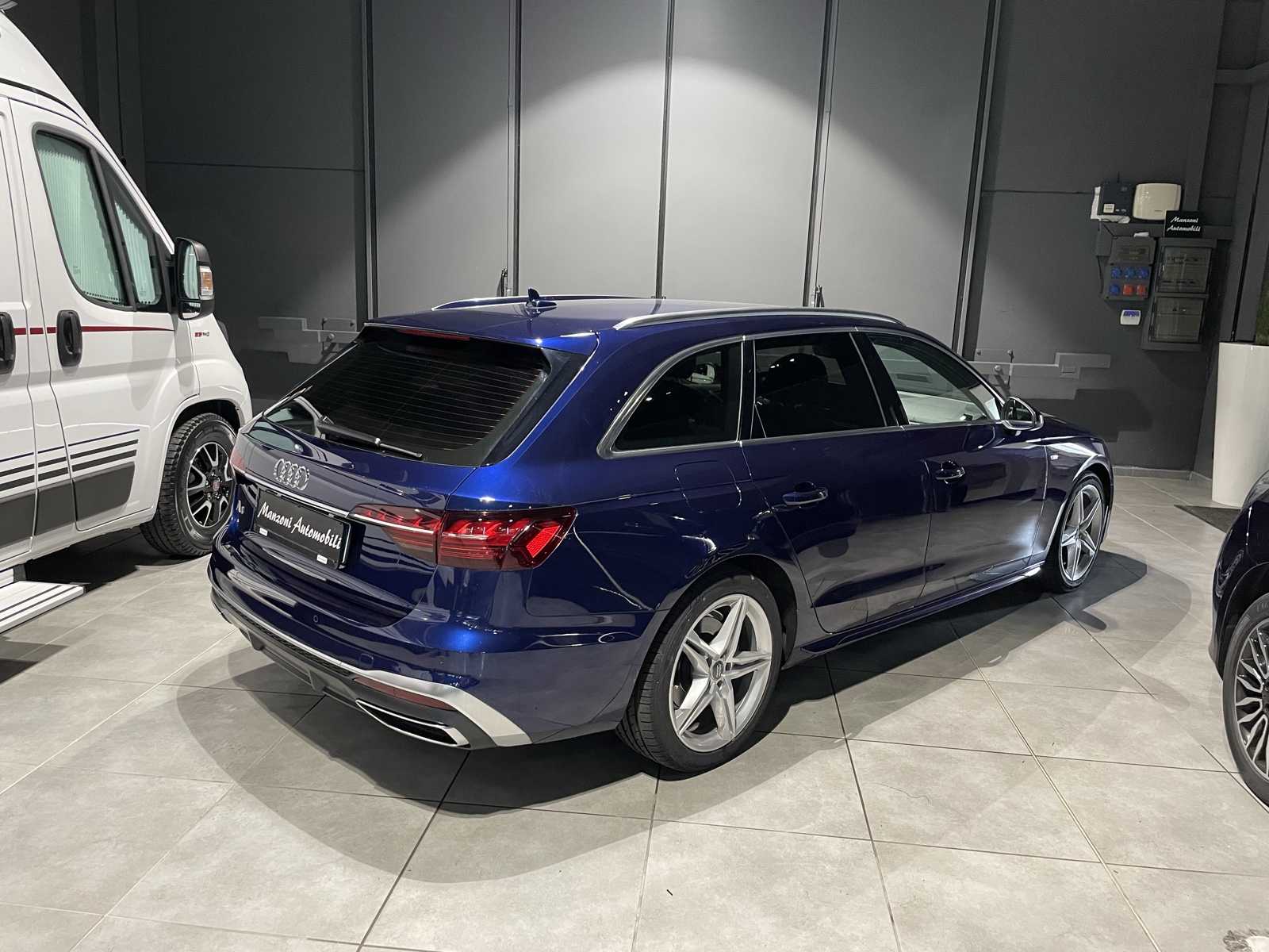 Audi station wagon blu fotografata di tre quarti posteriore in officina con lunotto e finestrini posteriori scuri.