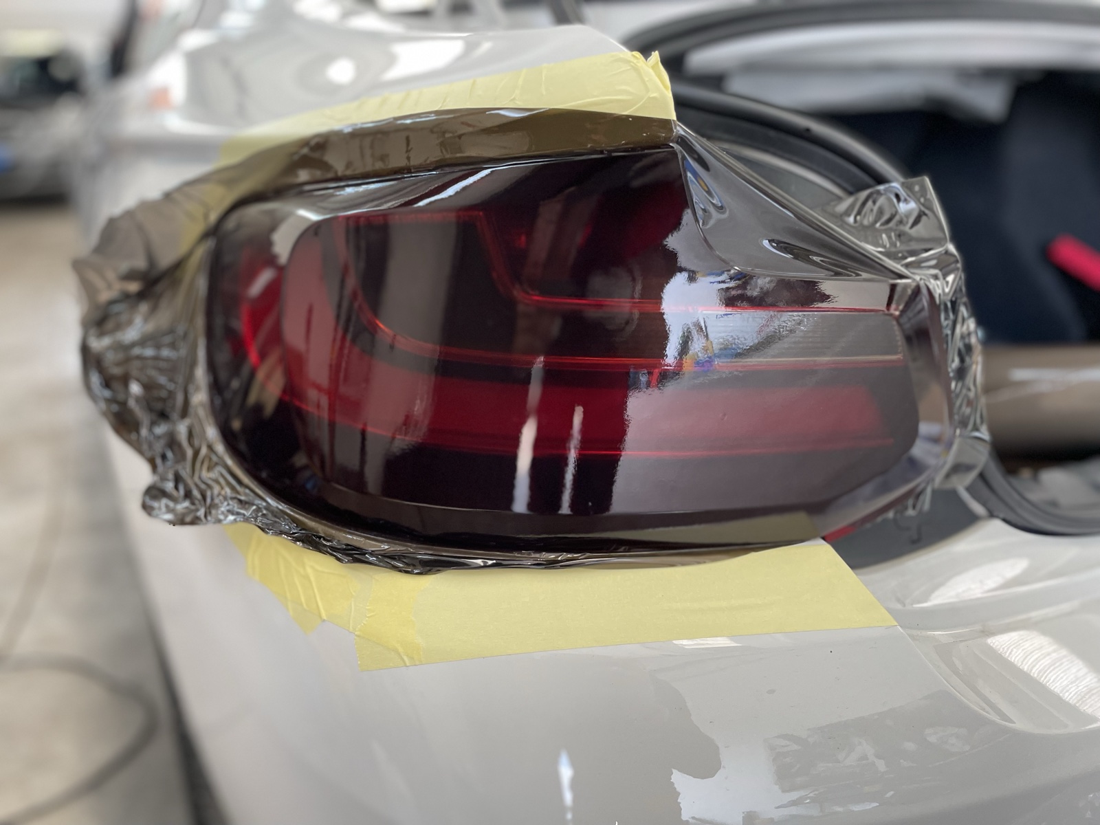 Dettaglio di un faro posteriore BMW con pellicola durante l’applicazione e nastro di mascheratura lungo i bordi.