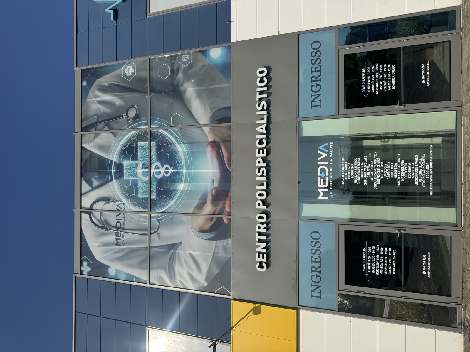 Facciata del centro polispecialistico Mediva con grande grafica sanitaria, insegna e scritte informative sui vetri degli ingressi.