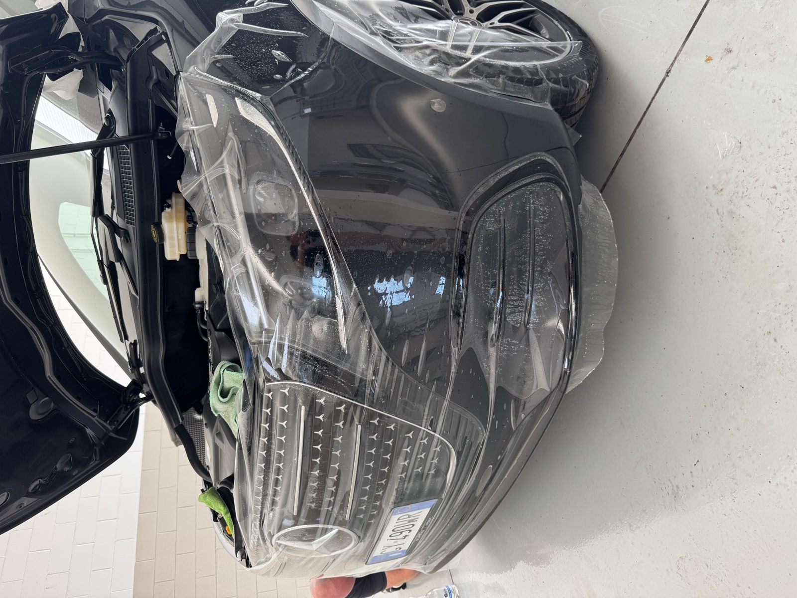 Applicazione di una pellicola trasparente sul paraurti, sul faro e sulla parte anteriore di un van Mercedes nero in officina.