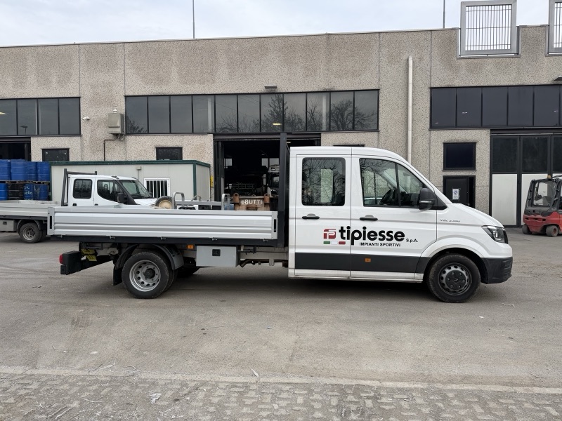 Autocarro bianco con cassone aperto e logo Tipiesse sulle portiere, fotografato di profilo davanti a un capannone.