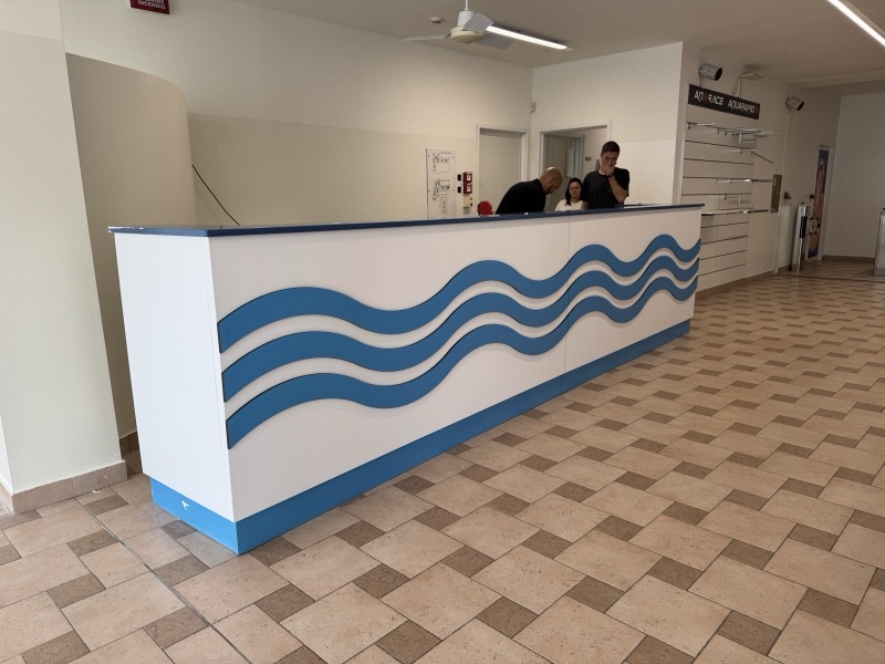 Bancone reception bianco decorato sul fronte con tre linee ondulate blu e una fascia blu alla base.