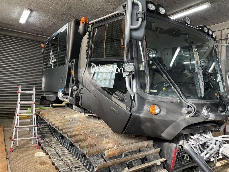 Mezzo cingolato grigio in officina con grafiche bianche Moncler Grenoble sul vano posteriore e scritta Chetzeron sulla cabina.