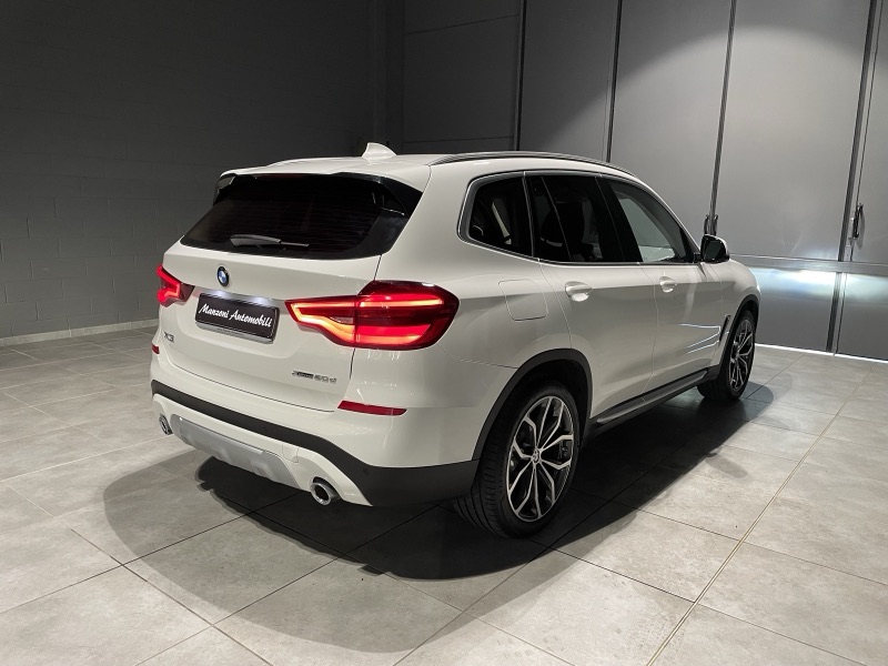 SUV BMW bianca fotografata di tre quarti posteriore in officina, con lunotto e finestrini posteriori scuri.