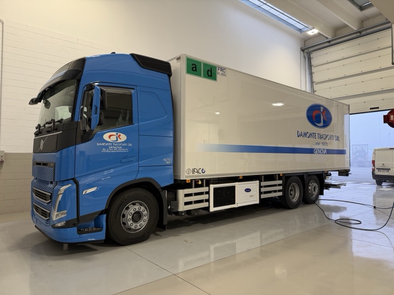 Camion con cabina blu e cassone bianco decorato con logo Lambrate Trasporti e fasce azzurre.