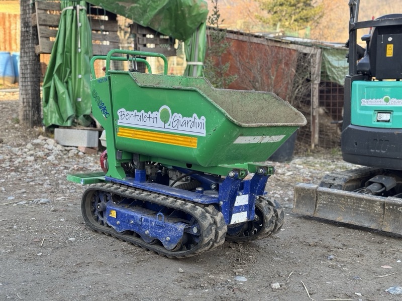 Piccolo dumper cingolato verde e blu con logo aziendale e fasce gialle applicati sul cassone.