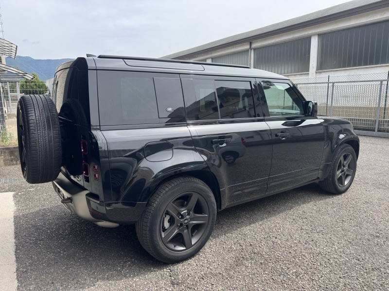 Land Rover Defender scuro di tre quarti posteriore all’esterno dell’officina con vetratura posteriore oscurata.
