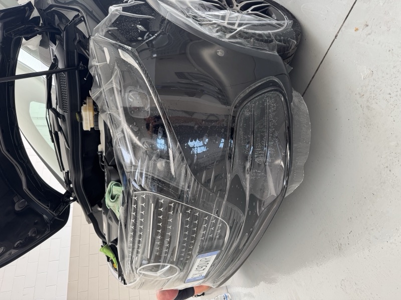 Applicazione di una pellicola trasparente sul paraurti, sul faro e sulla parte anteriore di un van Mercedes nero in officina.