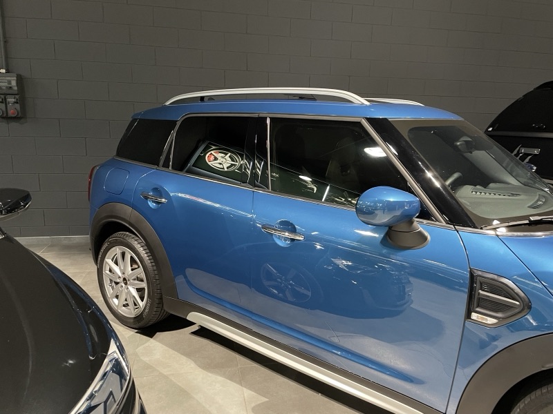 Mini Countryman blu fotografata di lato in officina, con finestrini posteriori oscurati e tetto a contrasto.