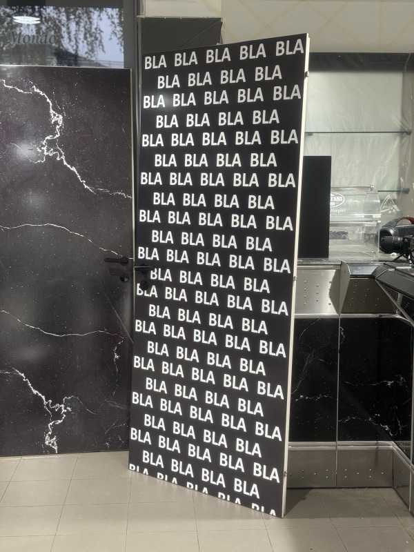 Pilastro interno con rivestimento nero e scritta BLA ripetuta in bianco, accanto a superfici scure effetto marmo.