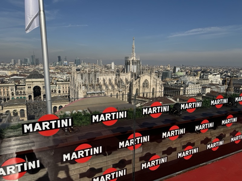 Grafiche Martini ripetute sui pannelli in vetro di una terrazza panoramica con lo skyline di Milano sullo sfondo.