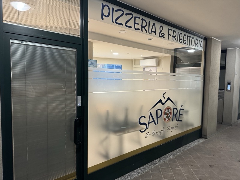 Vetrina della pizzeria Saporé con fascia satinata, righe orizzontali e logo blu.