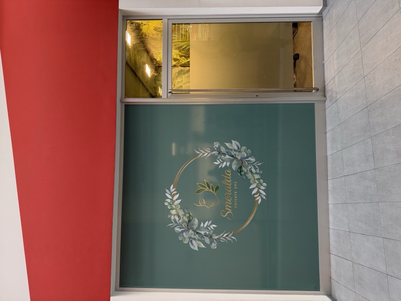 Vetrina con fondo verde opaco e decorazione circolare di foglie bianche e dettagli dorati sotto una fascia rossa.